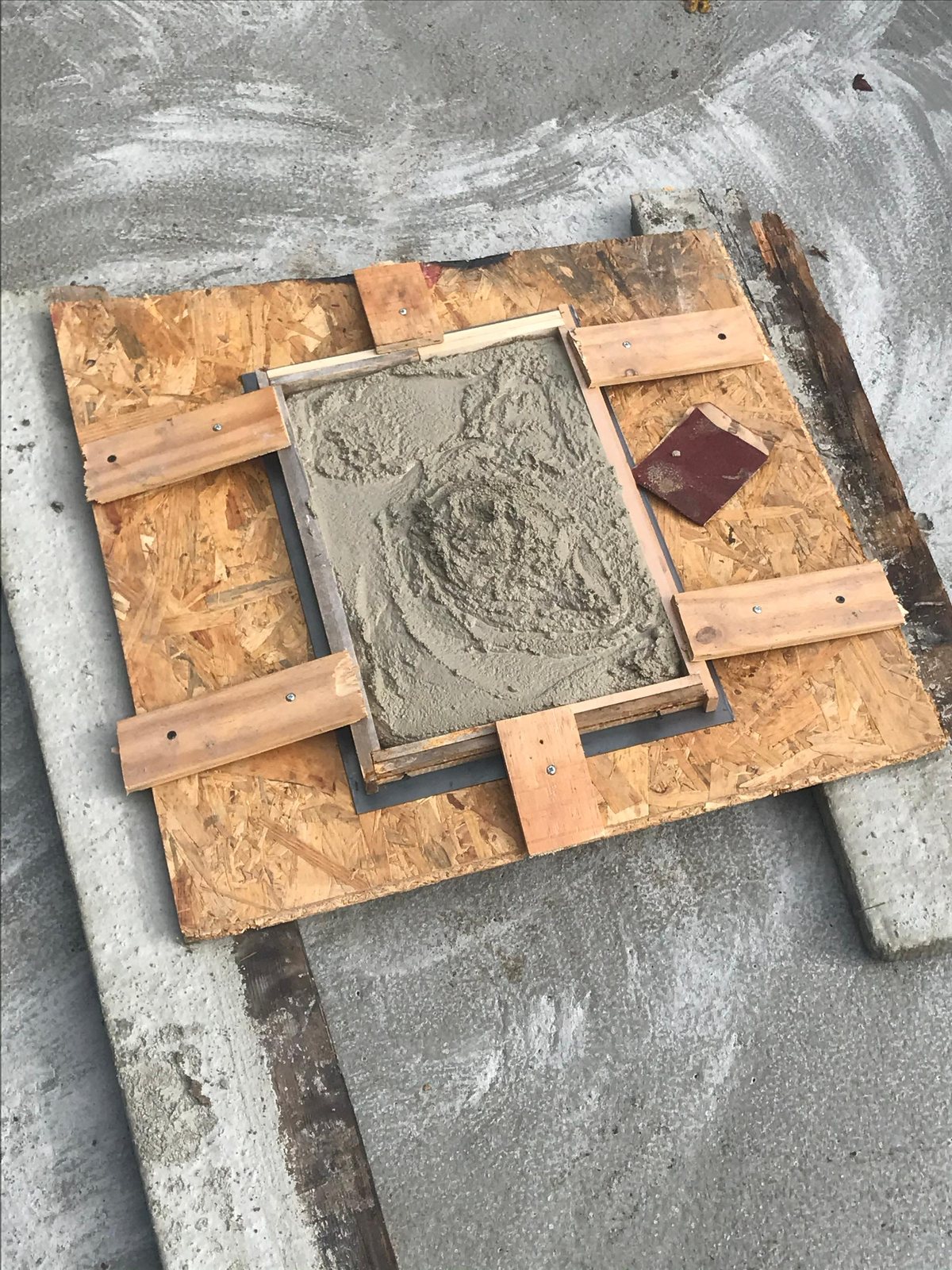 Coffrage de bois posé sur une dalle de béton, rempli de mortier frais encore lissé.